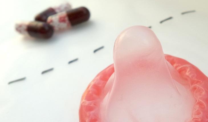 Na imagem, pílulas e uma camisinha rosa estão separados por tracejados em caneta. Consulta ginecológica.